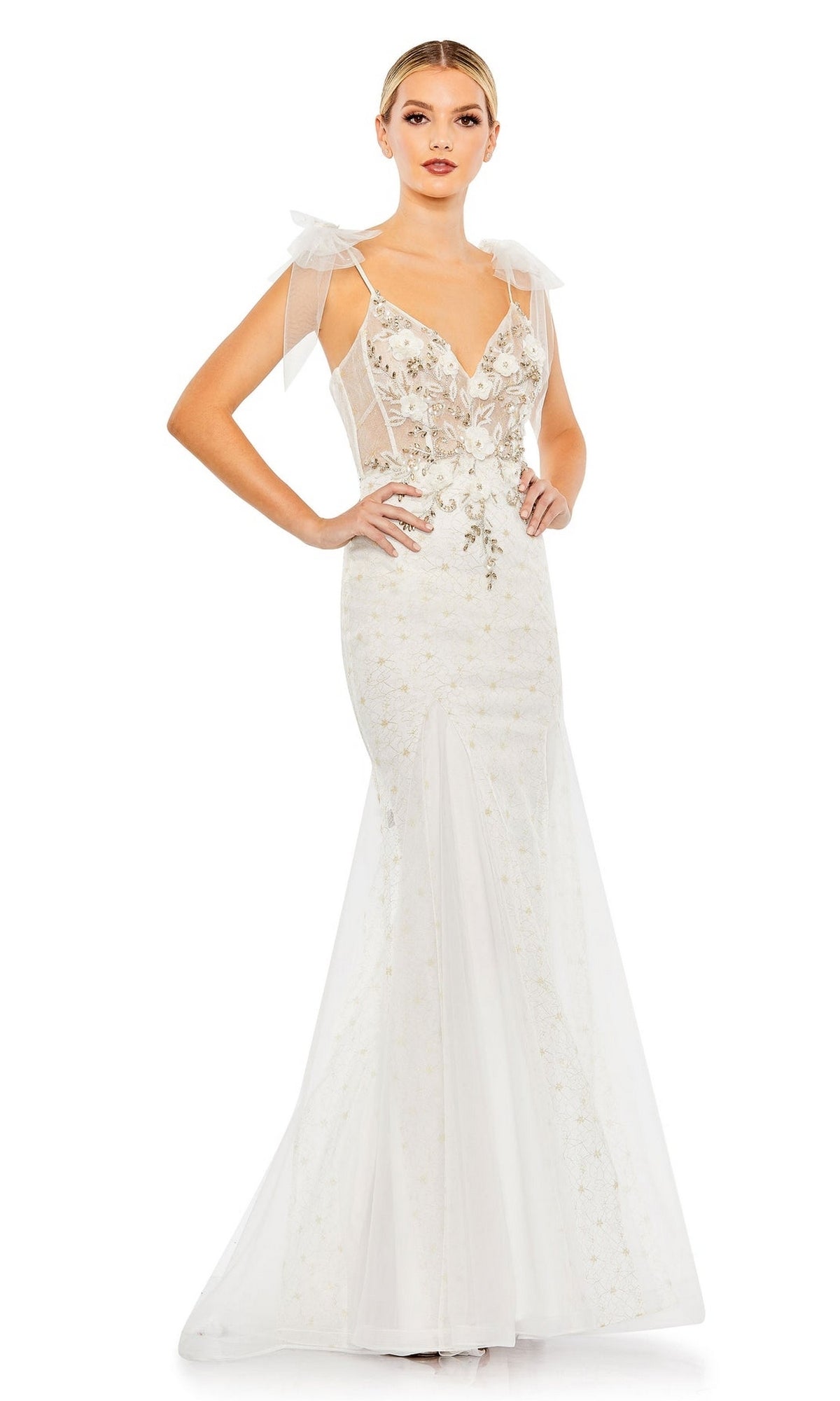 A woman poses with one hand on her hip against a white background, wearing the Long Formal Dress 50666 by Mac Duggal—a fitted, sleeveless white mermaid gown with floral embroidery and tulle shoulder bows.